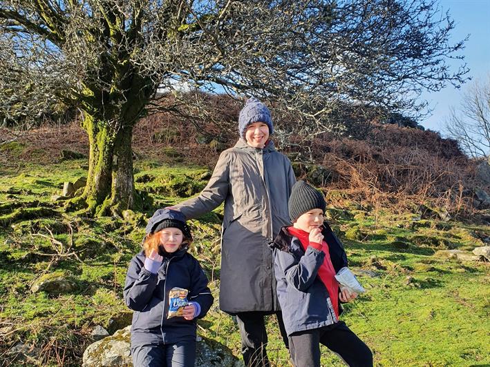 安妮和她的两个孩子在湖区的一座山坡上，正对着镜头微笑。 三人都戴着帽子和外套