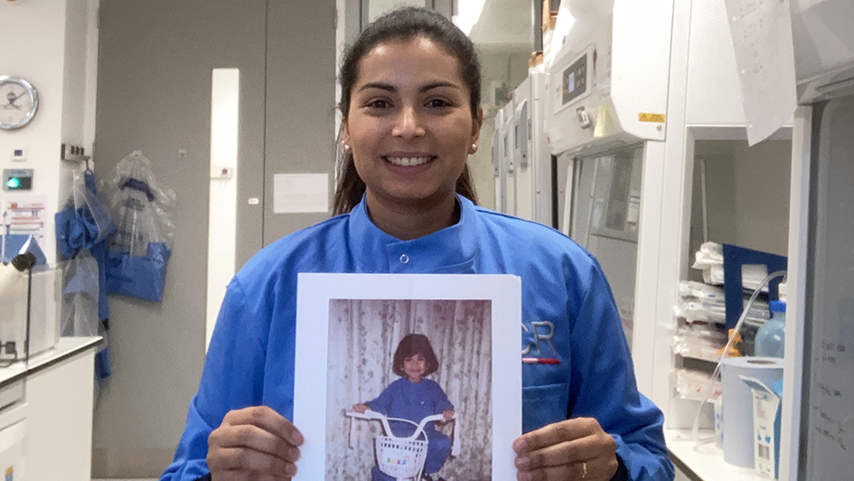 Erica Oliveira in the lab holding up a printed picture of herself as a kid