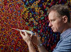 Artist James Cochran posing with a laboratory pipette in front of his painting 'Cell Defence'
