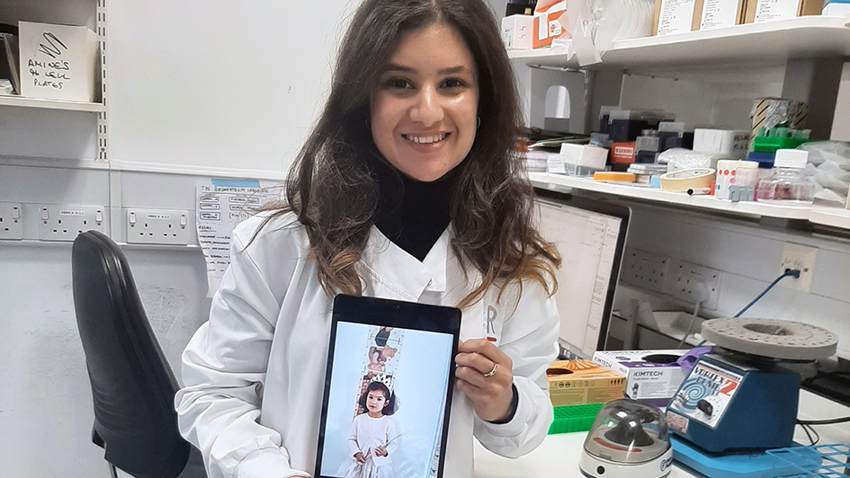 Melina Beykou in the lab holding up a printed picture of herself as a kid