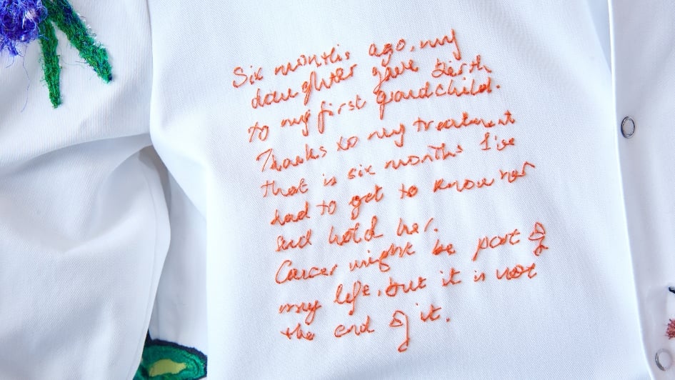 Close up of a patient's quote stitched on one of the lab coats with orange thread