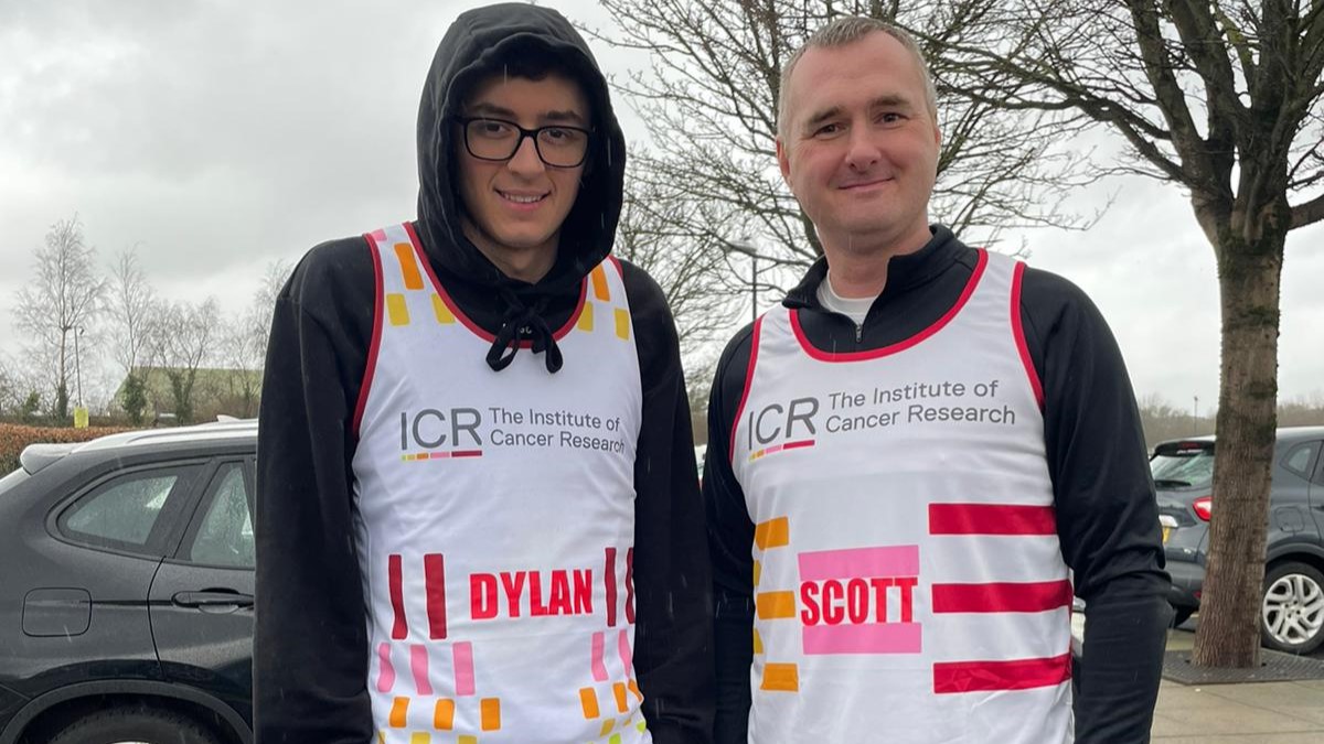 Dylan wearing a hoodie, glasses and an ICR vest stands in a car park next to his Dad Scott, wearing an ICR vest. They're both smiling into the camera