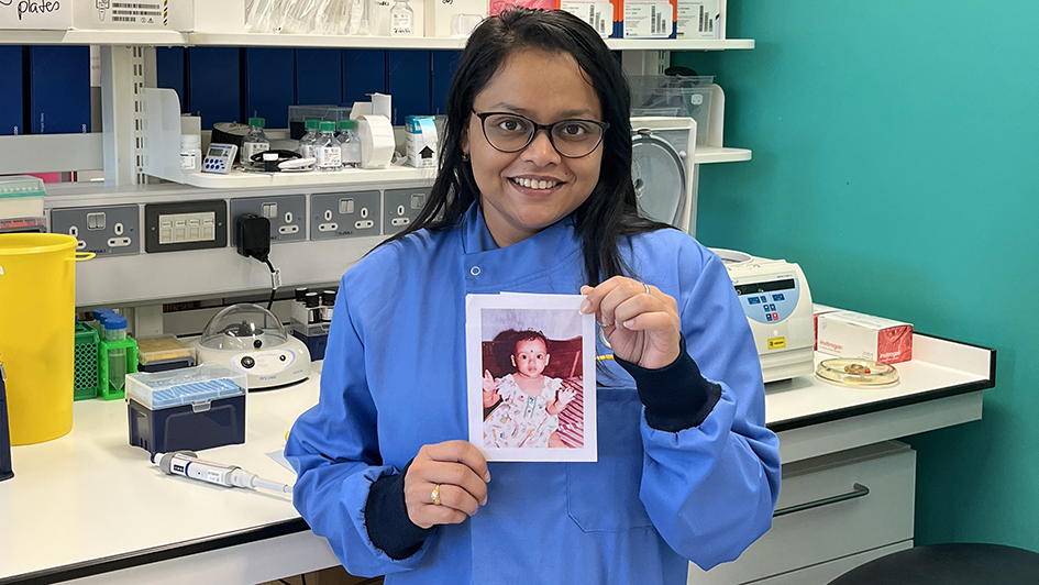 Supriti Ghosh in the lab holding up a printed picture of herself as a kid